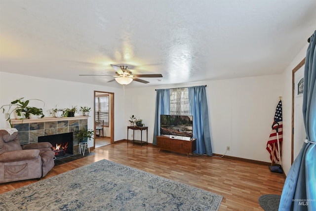 living room featuring ceiling fan, a fireplace, wood-type flooring, and a textured ceiling