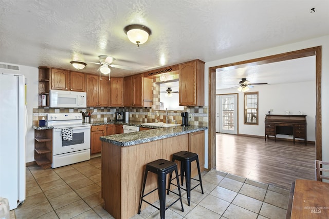 kitchen with kitchen peninsula, tasteful backsplash, white appliances, sink, and light tile patterned floors