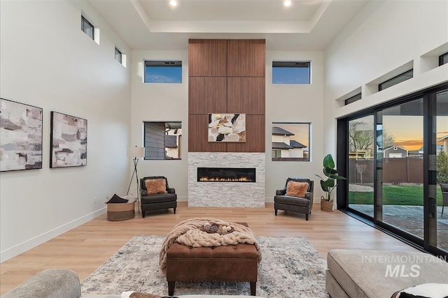 9891 W Napier Ct, Star, ID 83669 - living room featuring a raised ceiling, a glass covered fireplace, baseboards, light wood-type flooring, and a towering ceiling
