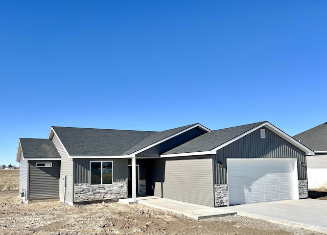 ranch-style house with stone siding, roof with shingles, an attached garage, and driveway