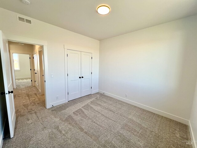 unfurnished bedroom featuring baseboards, visible vents, a closet, and light colored carpet