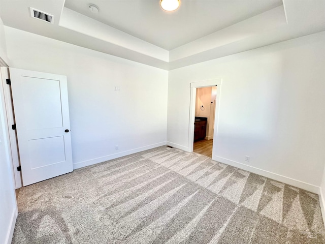 spare room with carpet floors, a raised ceiling, visible vents, and baseboards