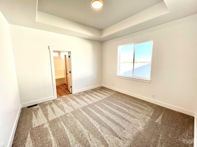 carpeted spare room with a tray ceiling, visible vents, and baseboards