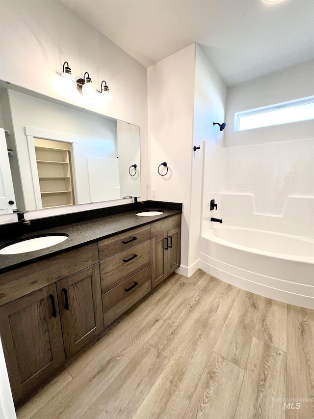 bathroom featuring double vanity, baseboards, wood finished floors, shower / bathtub combination, and a sink