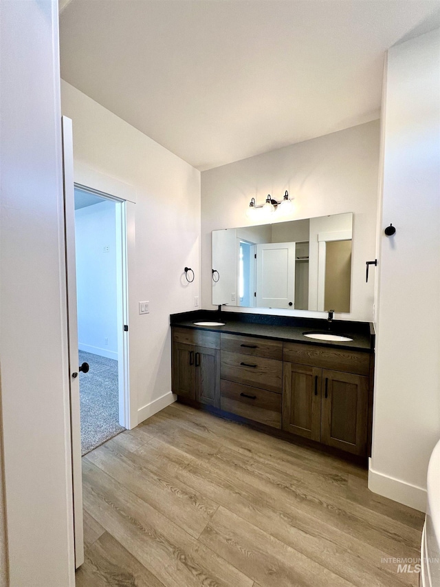 bathroom featuring wood finished floors, a sink, baseboards, and double vanity