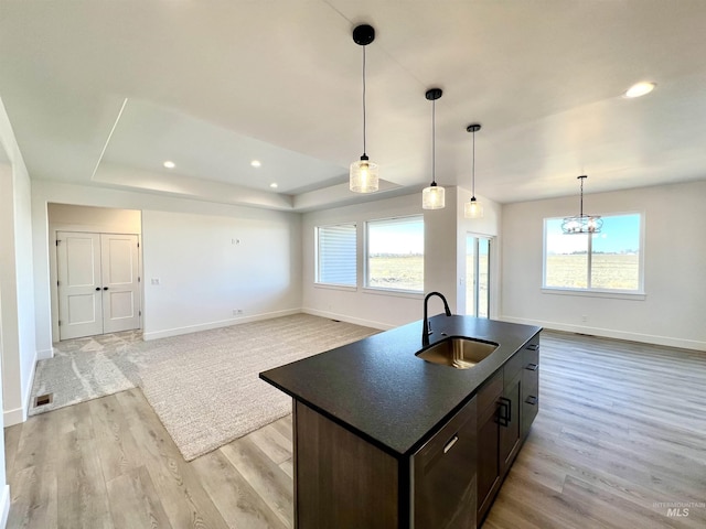 kitchen featuring a sink, visible vents, light wood-style floors, a tray ceiling, and dark countertops