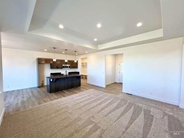 kitchen featuring a sink, open floor plan, stainless steel microwave, dark countertops, and a raised ceiling