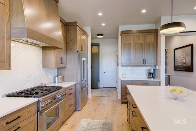 kitchen with wall chimney range hood, high end appliances, light wood-type flooring, and light countertops