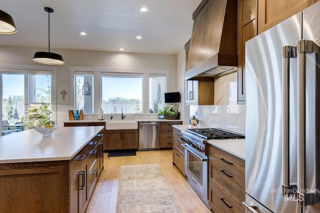 kitchen featuring light wood-style floors, high end appliances, custom exhaust hood, light countertops, and a sink
