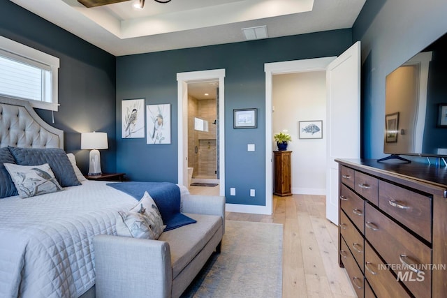 bedroom with baseboards, connected bathroom, visible vents, a tray ceiling, and light wood finished floors