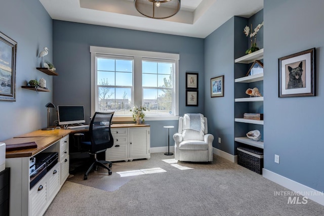 home office with baseboards, a raised ceiling, and light colored carpet