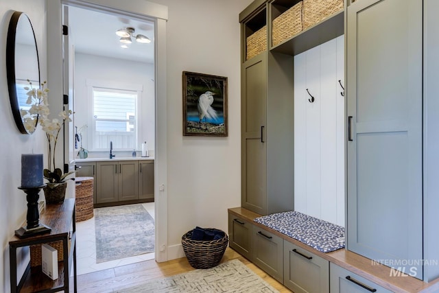mudroom featuring light wood-style flooring, a sink, and baseboards