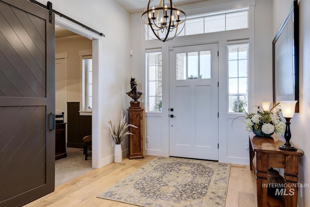 entryway with a barn door, a chandelier, and wood finished floors