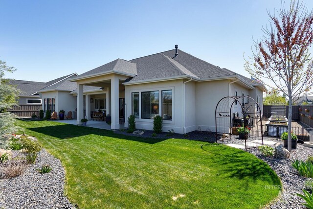 rear view of house featuring a patio, roof with shingles, stucco siding, fence, and a lawn