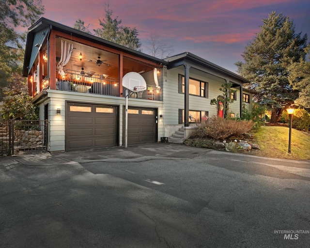 view of front of property featuring an attached garage, a balcony, fence, a ceiling fan, and driveway