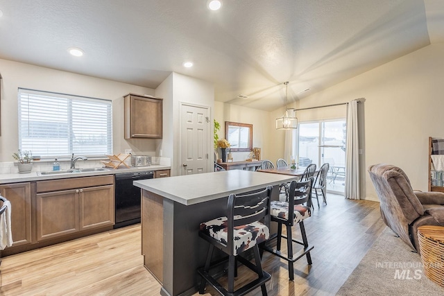 kitchen with a kitchen bar, black dishwasher, a sink, light wood-style floors, and vaulted ceiling