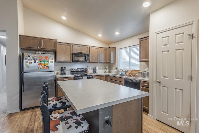 kitchen featuring a kitchen island, a breakfast bar, lofted ceiling, light wood-type flooring, and black appliances