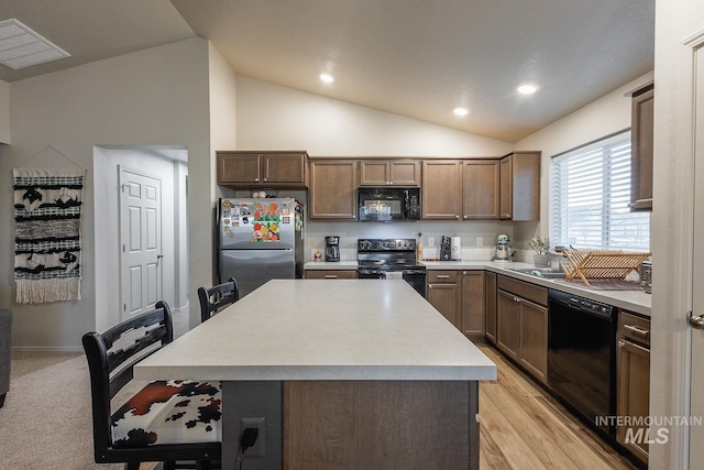 kitchen with light countertops, a kitchen bar, lofted ceiling, a center island, and black appliances