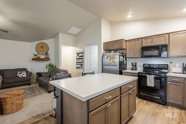 kitchen with open floor plan, black appliances, light wood-style flooring, and light countertops