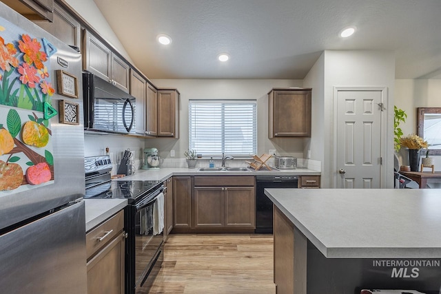 kitchen featuring light countertops, a sink, light wood finished floors, black appliances, and recessed lighting