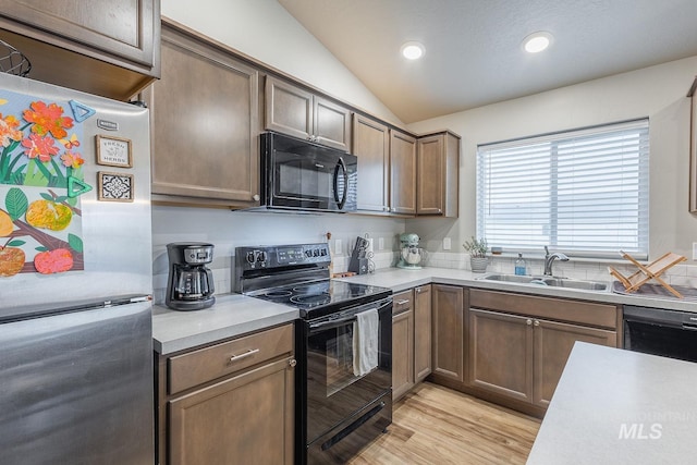 kitchen with vaulted ceiling, light countertops, a sink, light wood-style flooring, and black appliances