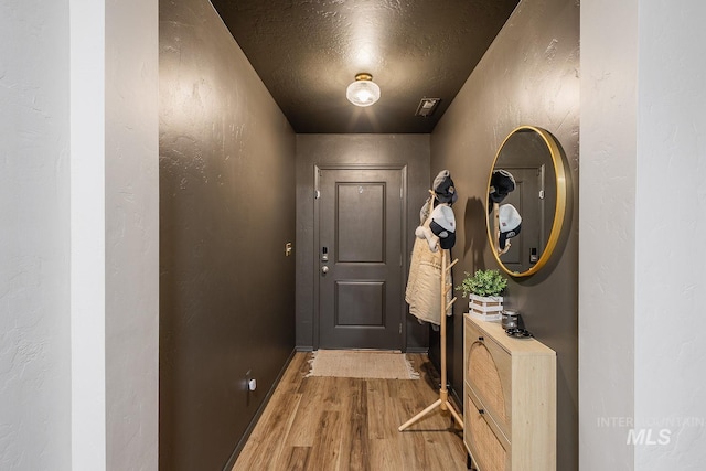 doorway with wood finished floors, a textured wall, and a textured ceiling