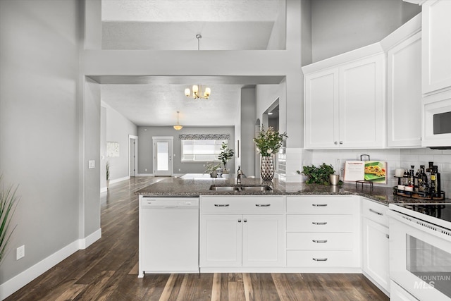 kitchen with white appliances, a sink, a peninsula, a chandelier, and white cabinets