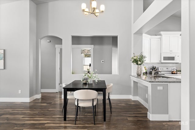 dining area featuring dark wood-style floors, arched walkways, a towering ceiling, a chandelier, and baseboards