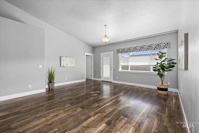 empty room with hardwood / wood-style flooring, a textured ceiling, baseboards, and vaulted ceiling