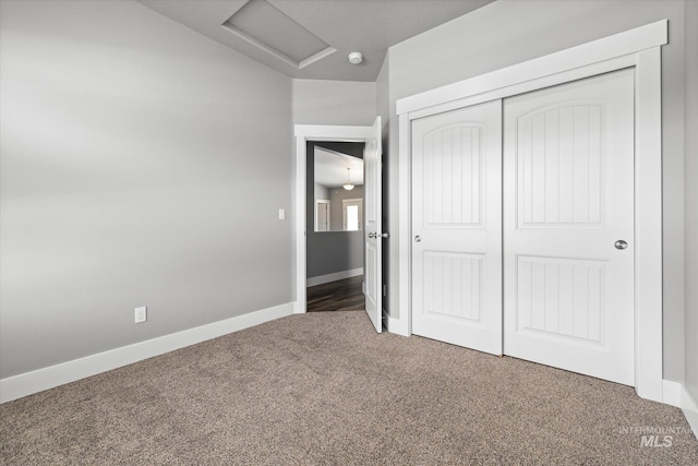 unfurnished bedroom featuring attic access, carpet, a closet, baseboards, and vaulted ceiling