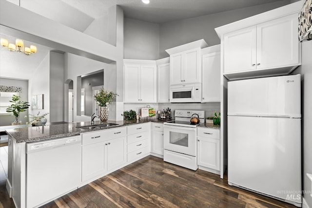 kitchen with white appliances, a sink, a peninsula, backsplash, and dark stone countertops