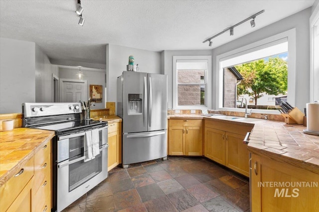 kitchen with sink, rail lighting, stainless steel appliances, tile counters, and a textured ceiling
