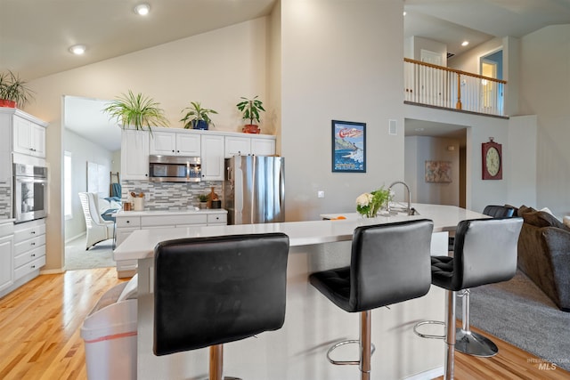 kitchen with white cabinets, a breakfast bar area, stainless steel appliances, light wood-type flooring, and high vaulted ceiling