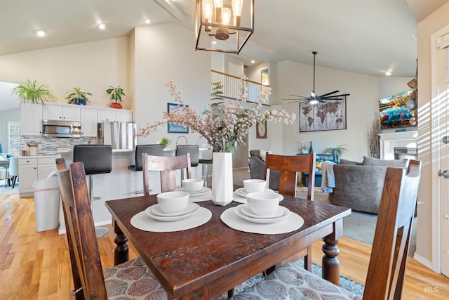 dining room featuring ceiling fan, high vaulted ceiling, light wood finished floors, and a tiled fireplace