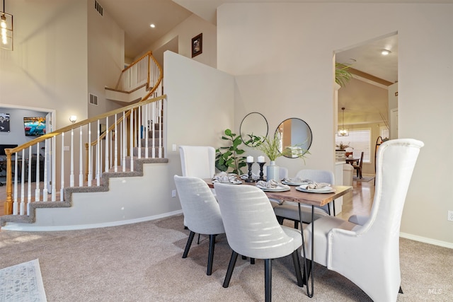 carpeted dining space with high vaulted ceiling, stairway, visible vents, and baseboards