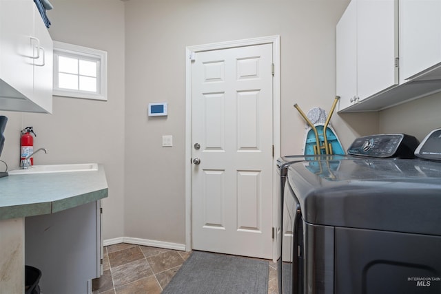 clothes washing area with cabinet space, baseboards, a sink, and washing machine and clothes dryer