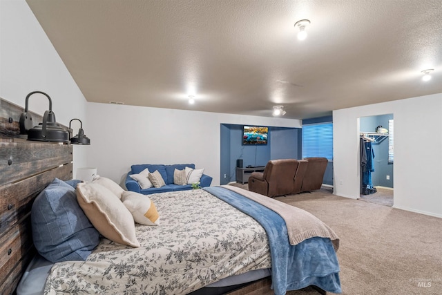 bedroom with a textured ceiling, carpet floors, a spacious closet, and baseboards