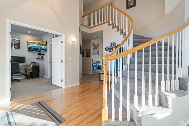 staircase featuring a high ceiling, wood finished floors, and baseboards