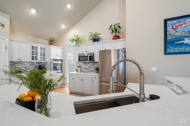 kitchen featuring stainless steel appliances, white cabinetry, light countertops, decorative backsplash, and glass insert cabinets