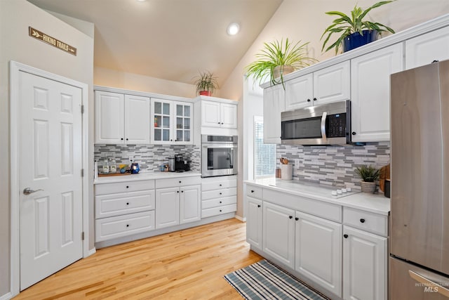 kitchen featuring lofted ceiling, stainless steel appliances, white cabinets, light countertops, and light wood finished floors