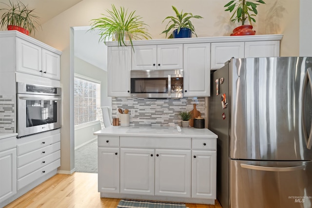 kitchen featuring stainless steel appliances, light countertops, decorative backsplash, and white cabinetry