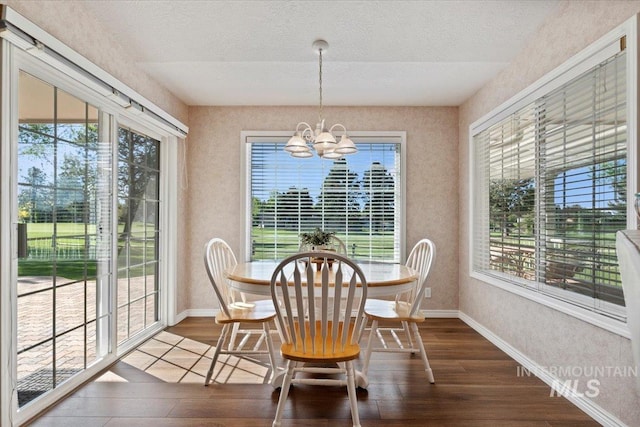dining space featuring dark wood-type flooring, a chandelier, baseboards, a textured ceiling, and a textured wall
