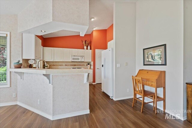 kitchen with white appliances, high vaulted ceiling, a peninsula, dark wood-style flooring, and light countertops
