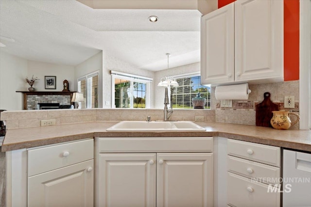kitchen with a sink, decorative backsplash, white cabinets, a fireplace, and light countertops