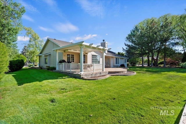 rear view of property featuring a chimney, a patio area, and a lawn