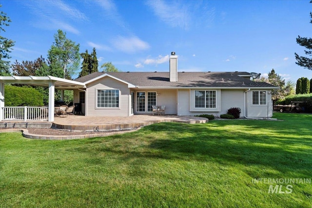 back of property with a chimney, a patio area, and a lawn