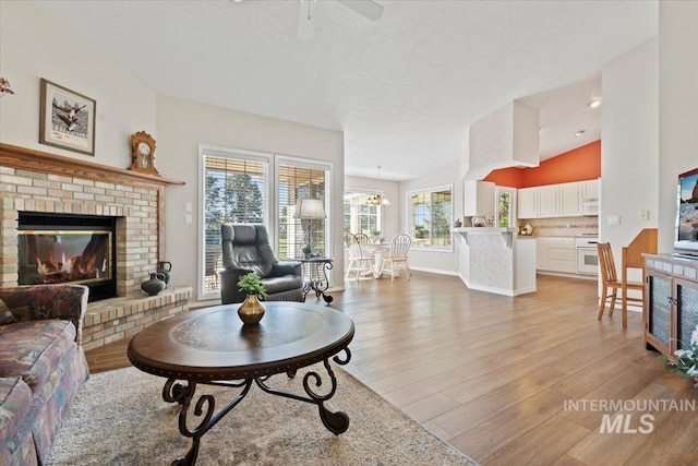 living area with light wood-type flooring, healthy amount of natural light, a brick fireplace, a ceiling fan, and vaulted ceiling