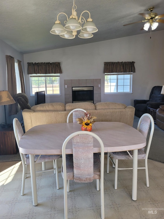 carpeted dining area with a textured ceiling, ceiling fan with notable chandelier, and a tile fireplace