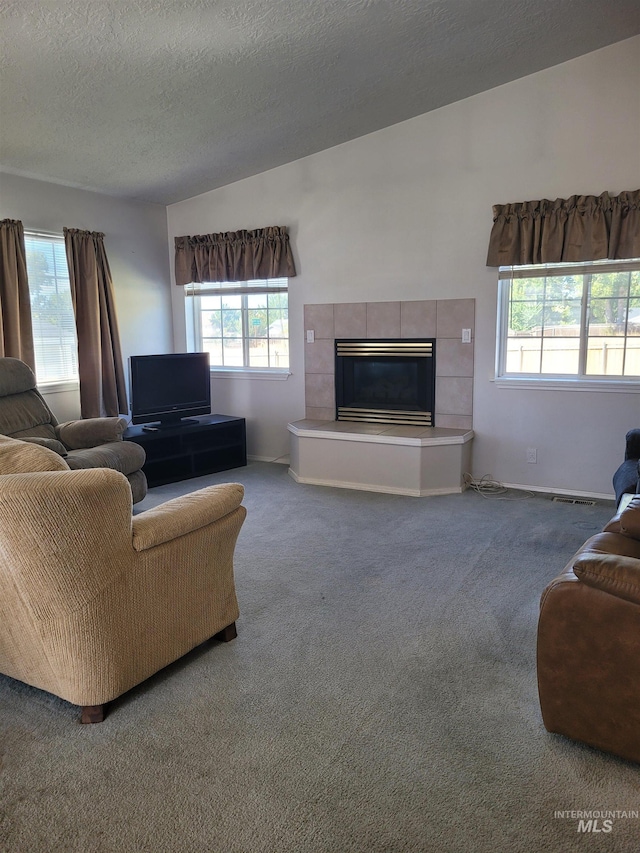 living room with a textured ceiling, carpet flooring, and a tiled fireplace