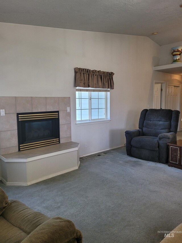 carpeted living room featuring a textured ceiling, a tiled fireplace, and vaulted ceiling